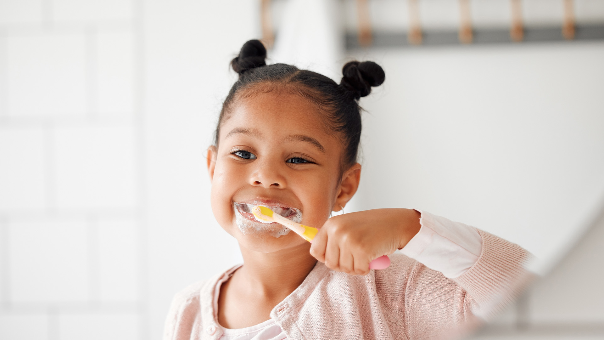 Children's Oral Hygiene at Home. A happy toddler brushes her teeth in the mirror.