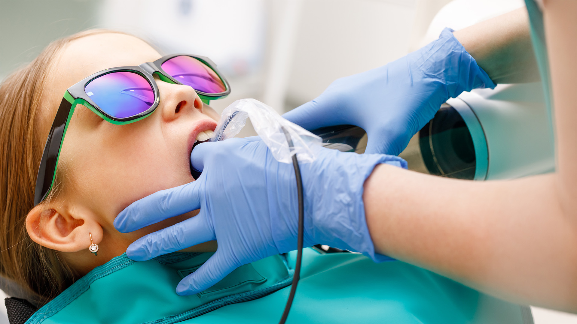 Digital X-Rays. A child wears sunglasses and lies back in the dentist's chair while the dentist takes x-rays.