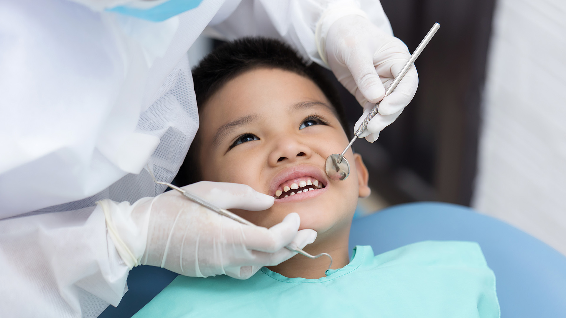 Pediatric Dental Exam. A child smiles and looks up from the dentist's chair as he receives is dental exam.