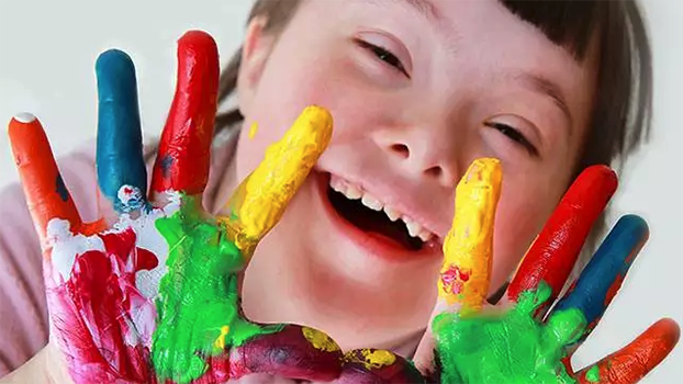 Special Needs Dental Care. A smiling special needs child hold her paint covered hands up to the camera for a picutre.