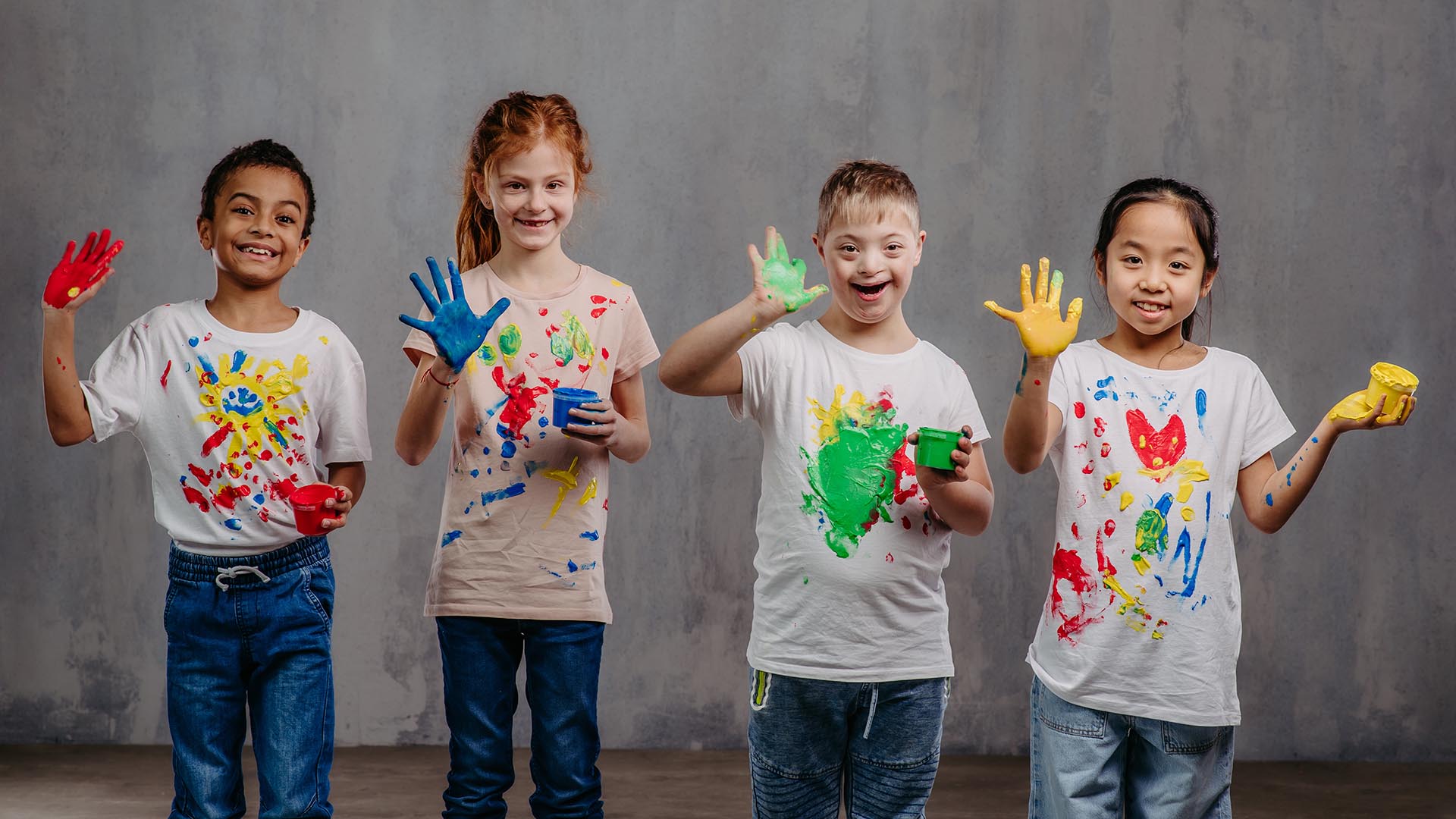 Special Needs Dentistry. A group of happy children wave their paint covered hands at the camera and smile.