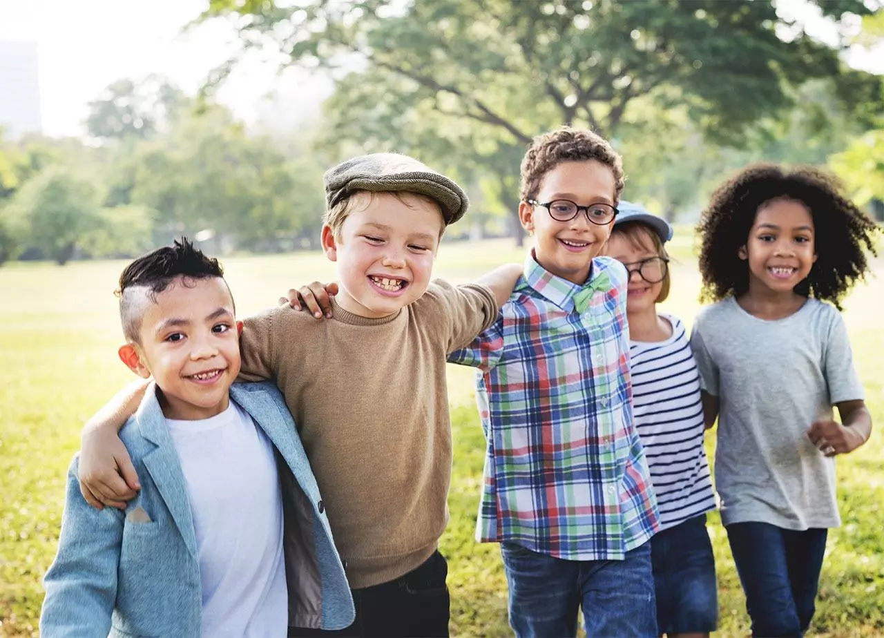 A group of children smile and walk through a park arm in arm. Confident smiles brought to you by Alabaster Smiles Pediatric Dentistry.