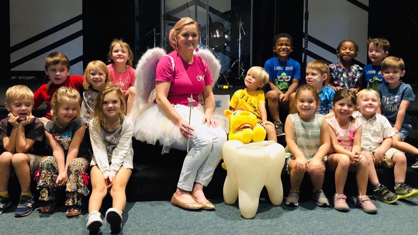 Educating Our Kids About Dental Health. A staff member dressed as the tooth fairy teaches a class of kids about healthy smiles.