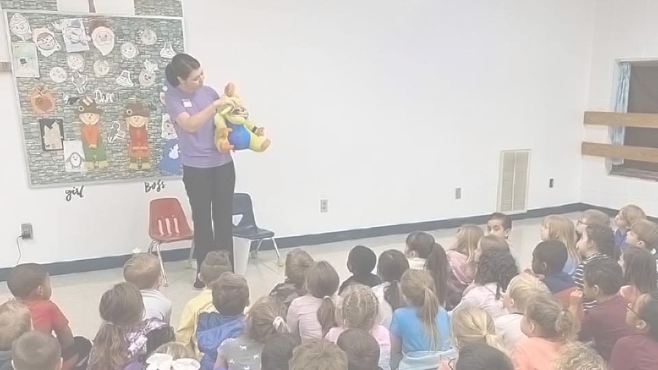 School Education Programs For Elementary. A member of the Alabaster Smiles staff demonstrates how to properly brush her teeth to a class of children.